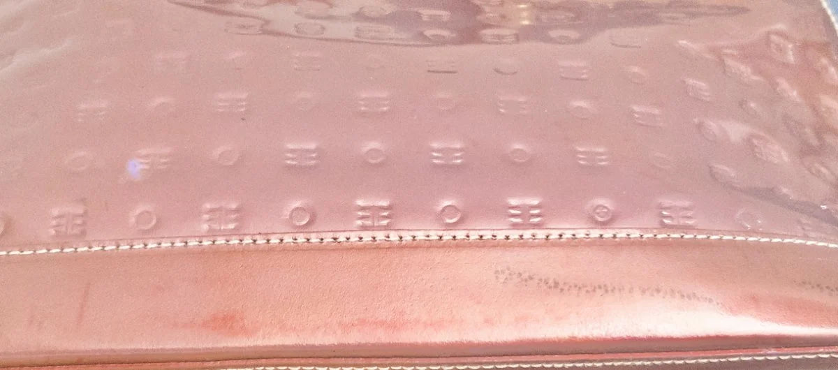 A close-up of a metallic rose gold clutch or wallet featuring an embossed monogram pattern and a stitched leather trim.